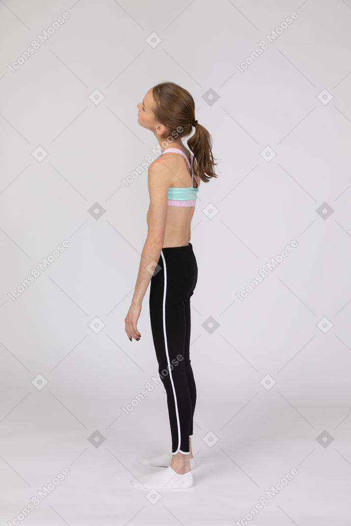 Vista lateral de una jovencita en ropa deportiva echando la cabeza hacia atrás