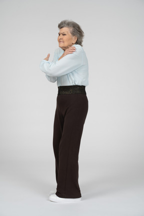 Elderly woman standing and hugging herself