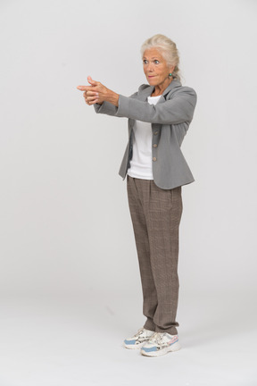 Seitenansicht einer alten dame im anzug, die eine waffe mit den fingern zeigt