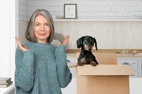 A woman standing in front of a box with a dachshund in it