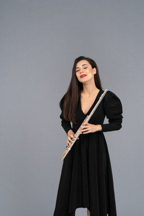 Вид спереди молодой леди в черном платье, держащей флейту