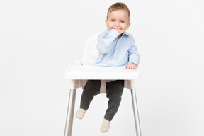 Adorable bebé sentado en una silla alta y tomados de la mano en la boca
