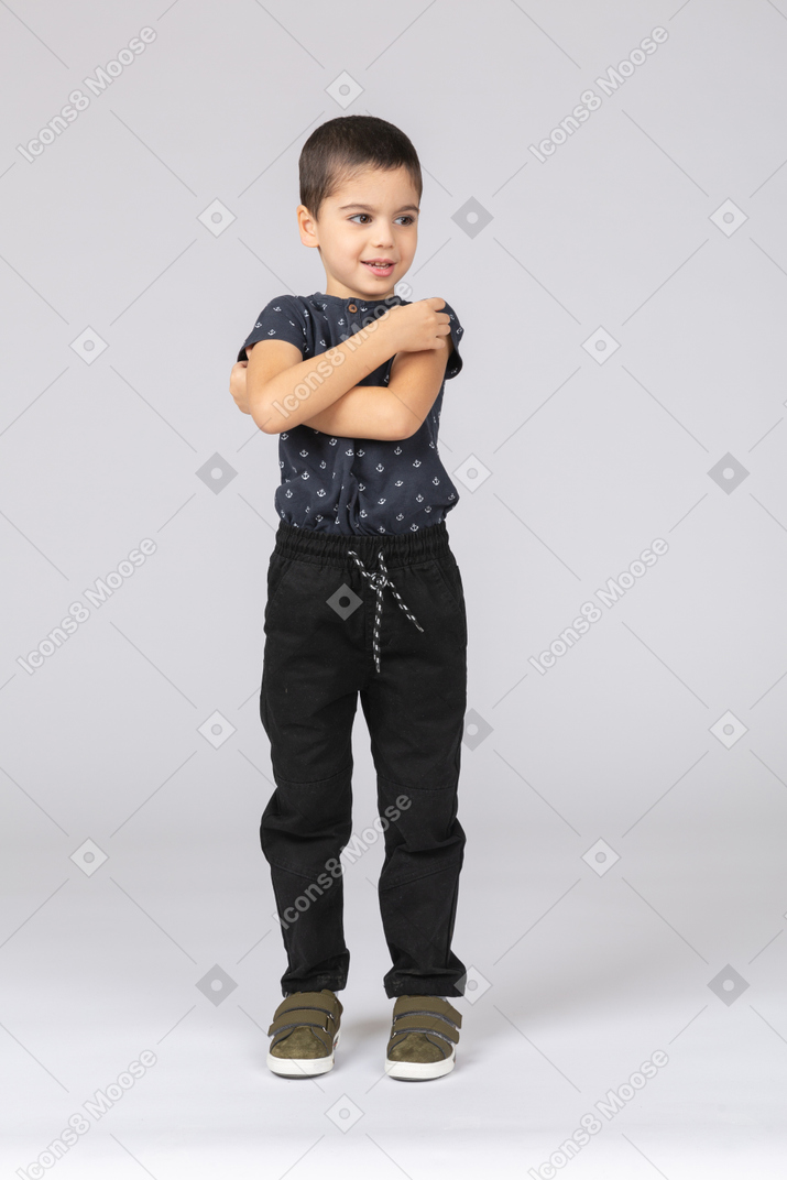 Vista frontal de um lindo menino em pé com os braços cruzados e olhando para o lado
