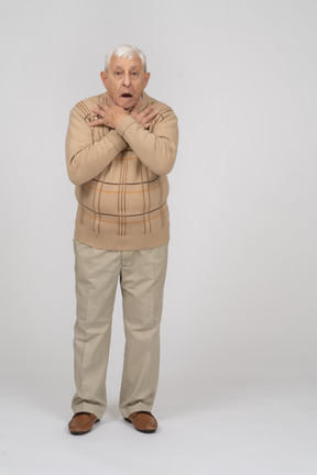 Front view of a scared old man in casual clothes standing with hands on shoulders