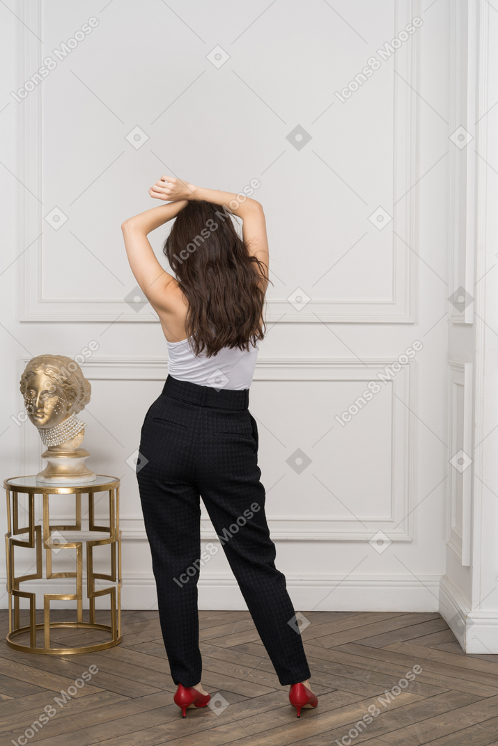 Back view of a young female raising hands while standing by a golden greek sculpture