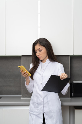 Vista lateral de una doctora ocupada sosteniendo su teléfono y una tableta