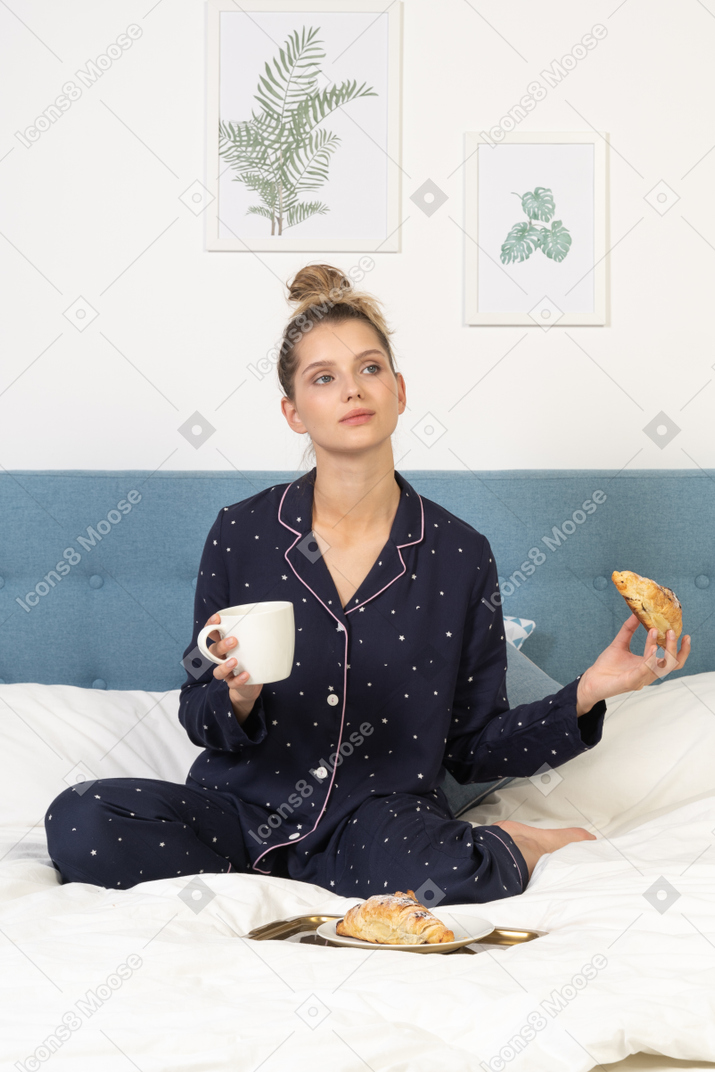 一位穿着睡衣的年轻女士在床上吃早餐的前视图