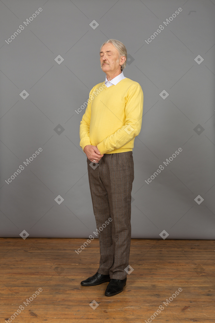 四分之三的视图的老人穿着黄色套头衫，手牵着手，闭着眼睛