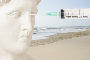 Riesiger statuenkopf mit spritze am strand