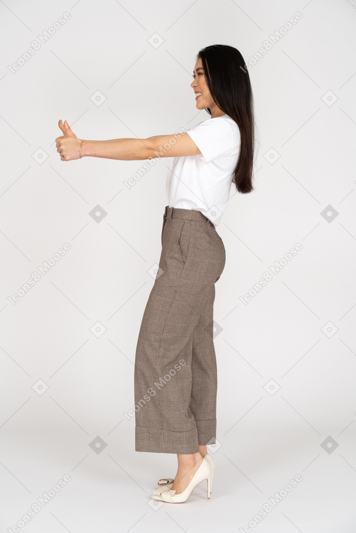 Vista lateral de uma jovem sorridente de calça e camiseta mostrando o polegar