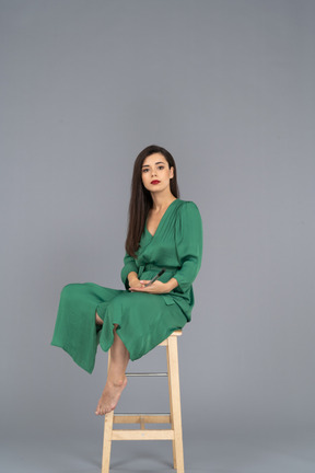 Девушка в зеленом платье в полный рост сидит на стуле с кларнетом в руке