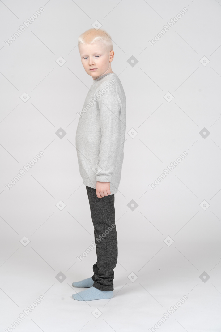 A blonde little boy in casual clothes standing thoughtfully