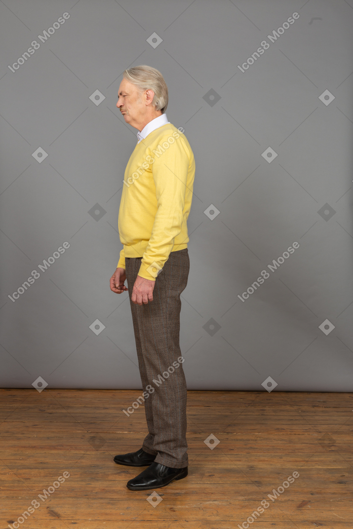 Vista laterale di un vecchio maschio scontento che indossa un pullover giallo e chiude gli occhi