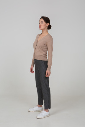 Вид в три четверти молодой леди, стоящей неподвижно в пуловере и штанах и смотрящей в сторону