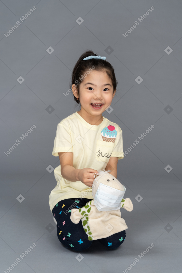 Cheerful little girl putting a face mask on a toy