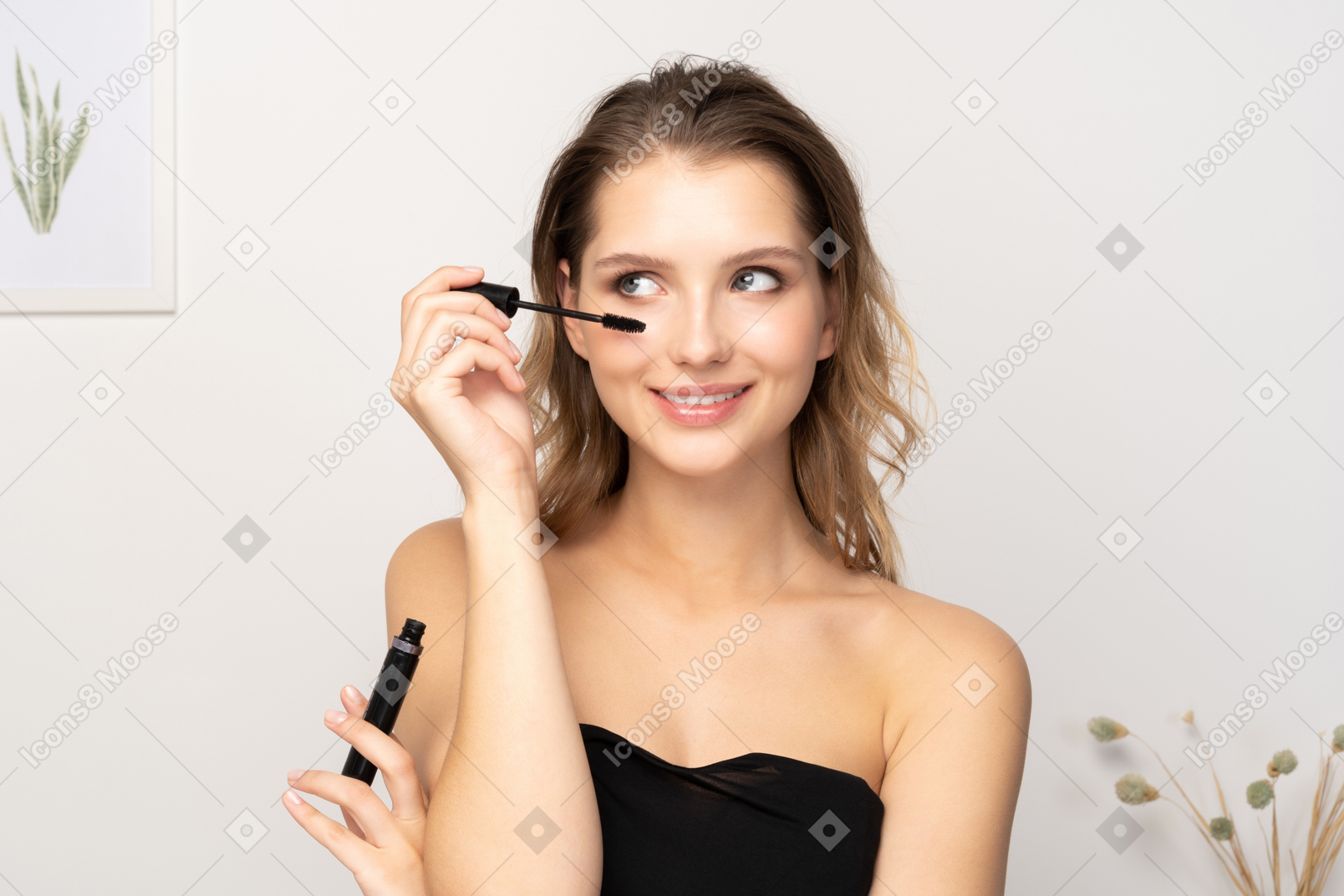 Front view of a smiling young woman wearing black top applying mascara