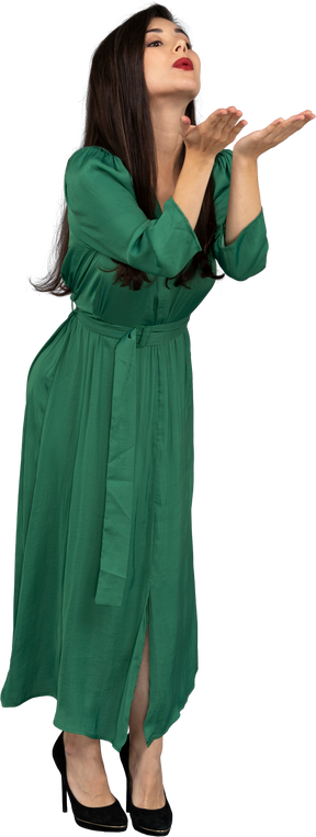 Vista de três quartos de uma jovem de vestido verde enviando um beijo no ar