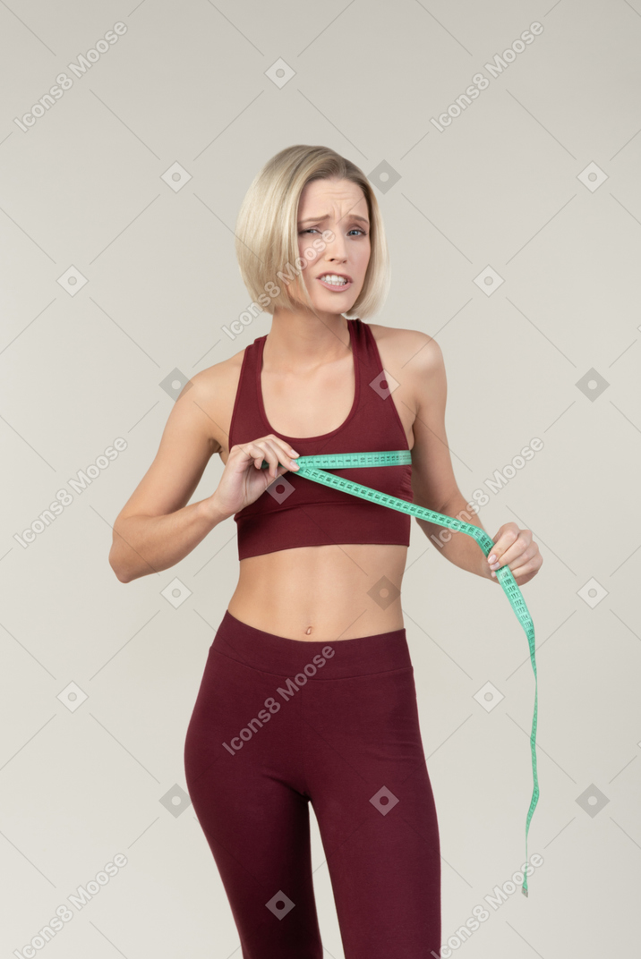 Sad looking woman in sportswear measuring chest