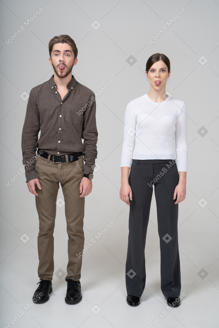 Vista frontal de um jovem casal com roupa de escritório, mostrando a língua
