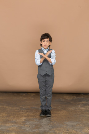 Vista frontal de um menino bonito de terno cinza, mostrando o sinal de pare