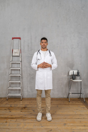 Front view of a young doctor standing in a room with ladder and chair