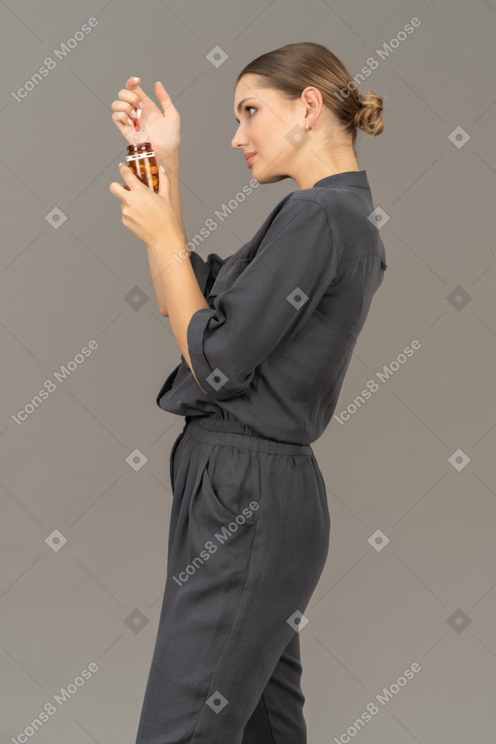 Vista lateral de uma jovem com um macacão olhando para os comprimidos em um frasco