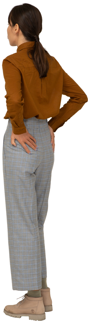 Vista traseira de três quartos de uma jovem mulher asiática fazendo beicinho de calça e blusa colocando as mãos nos quadris