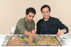 Two young interracial friends sitting at the table and playing board game
