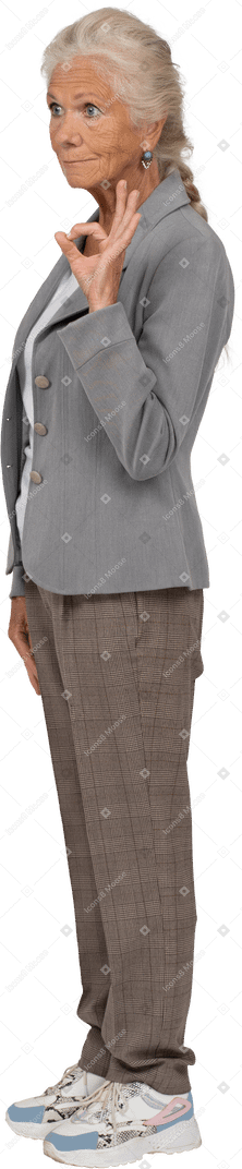 Vue latérale d'une vieille femme en veste grise montrant un signe ok