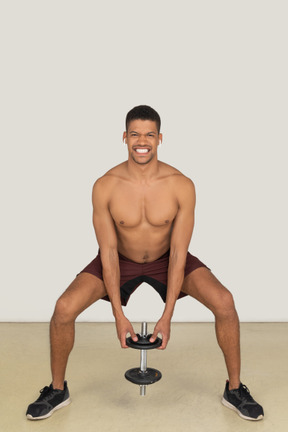 A frontal view of the handsome athletic man doing exercises squatting and smiling