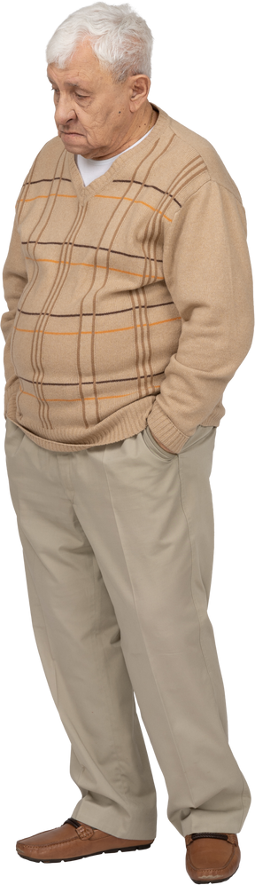 Vue de face d'un vieil homme en vêtements décontractés debout avec les mains dans les poches et regardant quelque chose avec intérêt