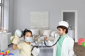 A little boy in lab coat with stethoscope standing next to a little girl in face mask