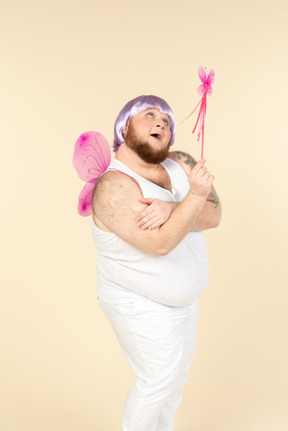 年轻超重的男人打扮成一位仙女抬头，拿着仙女魔杖