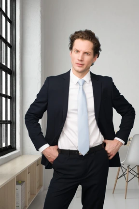 A man in a suit and tie standing in front of a window