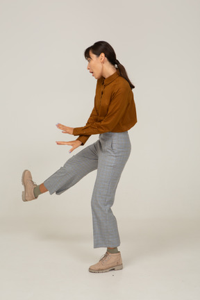 一位身着马裤和上衣抬腿跳舞的亚洲年轻女性的侧视图