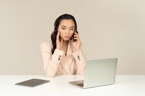 Asiatischer weiblicher büroangestellter, der mit telefonanruf gestört schaut