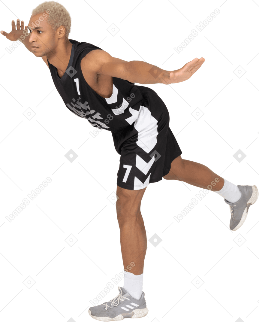 Vista di tre quarti di un giovane giocatore di basket maschile in equilibrio che si sporge in avanti e si trova su una gamba sola