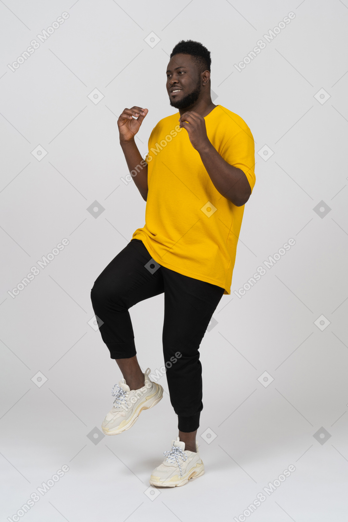 一个身穿黄色 t 恤、抬腿的黑皮肤年轻男子的四分之三视图