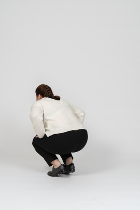 Rear view of a plump woman in casual clothes squatting