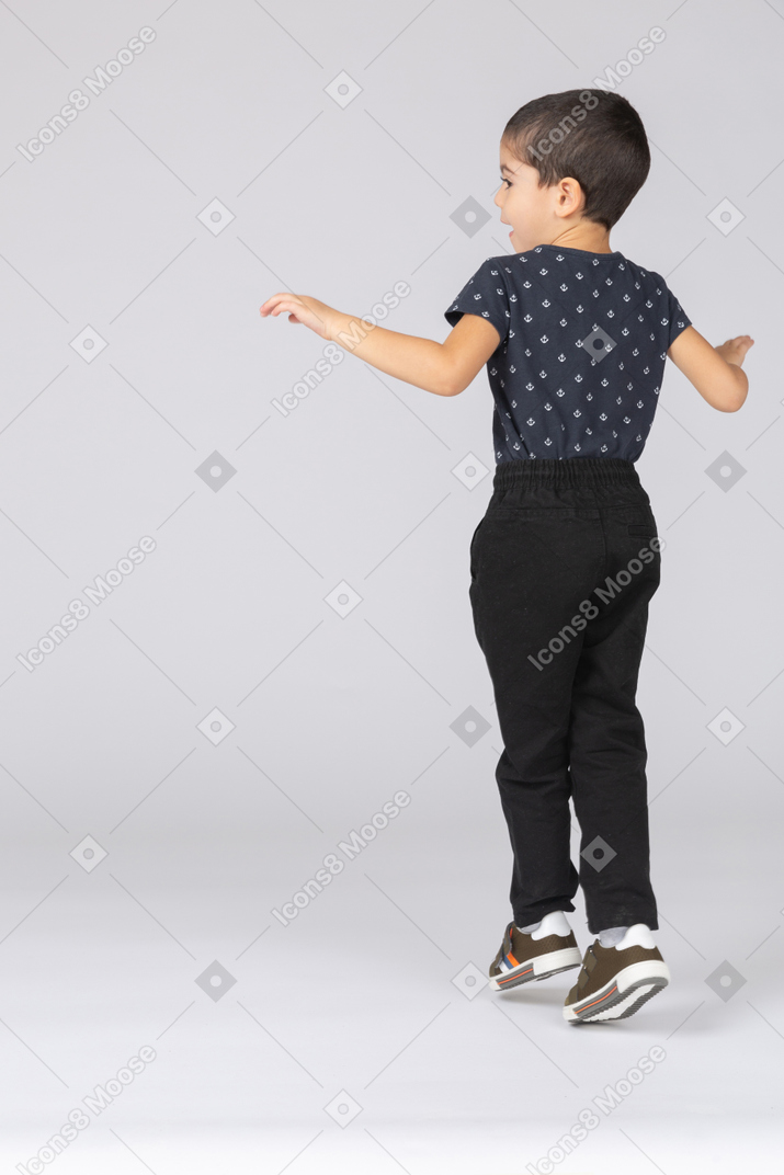 Rear view of a cute boy standing on toes and outstretching arms