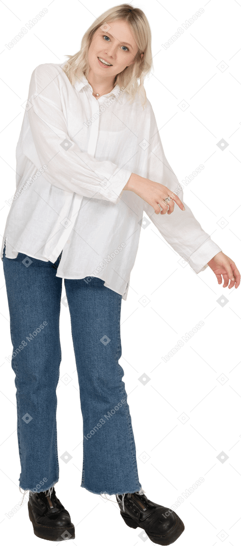 Vista frontale di una donna bionda in abiti casual che si fa da parte mentre tende le mani e guarda la fotocamera