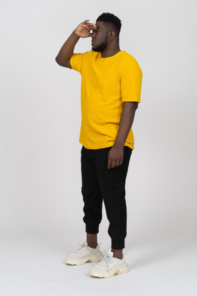 Vista di tre quarti di un giovane uomo dalla pelle scura in maglietta gialla che cerca qualcosa