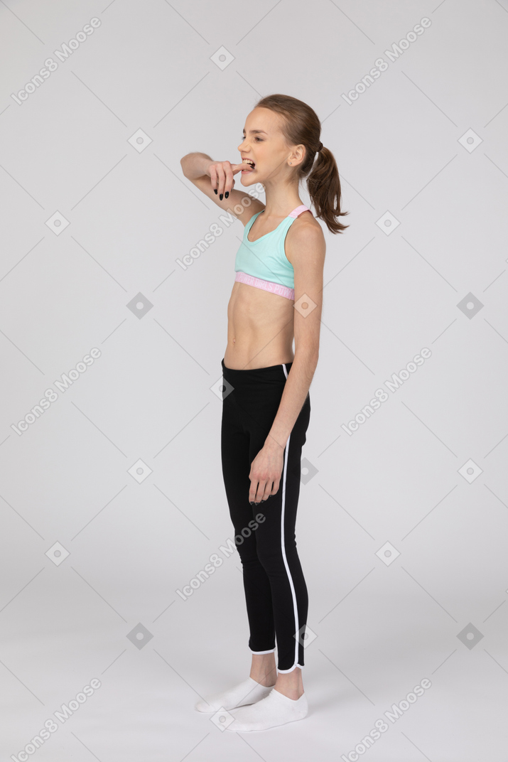 Three-quarter view of a teen girl in sportswear biting her finger