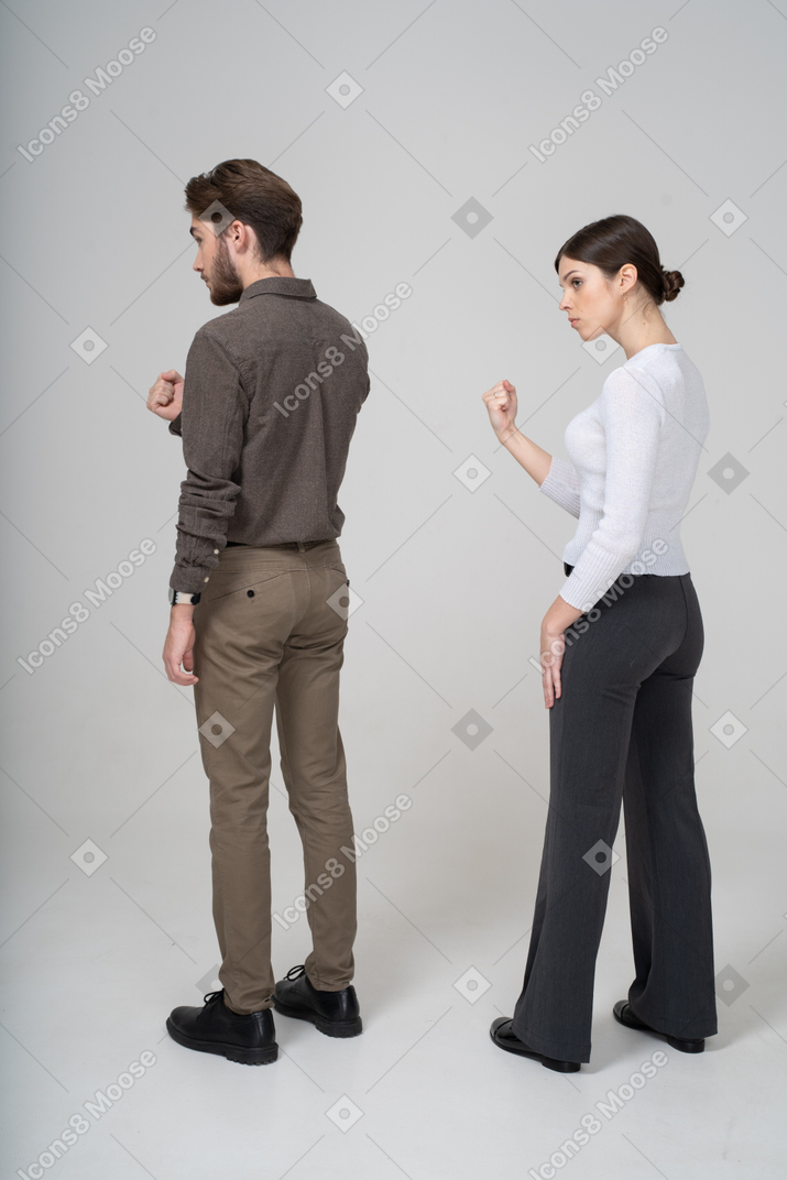 Vista posterior de tres cuartos de una estricta pareja joven en ropa de oficina mostrando el puño