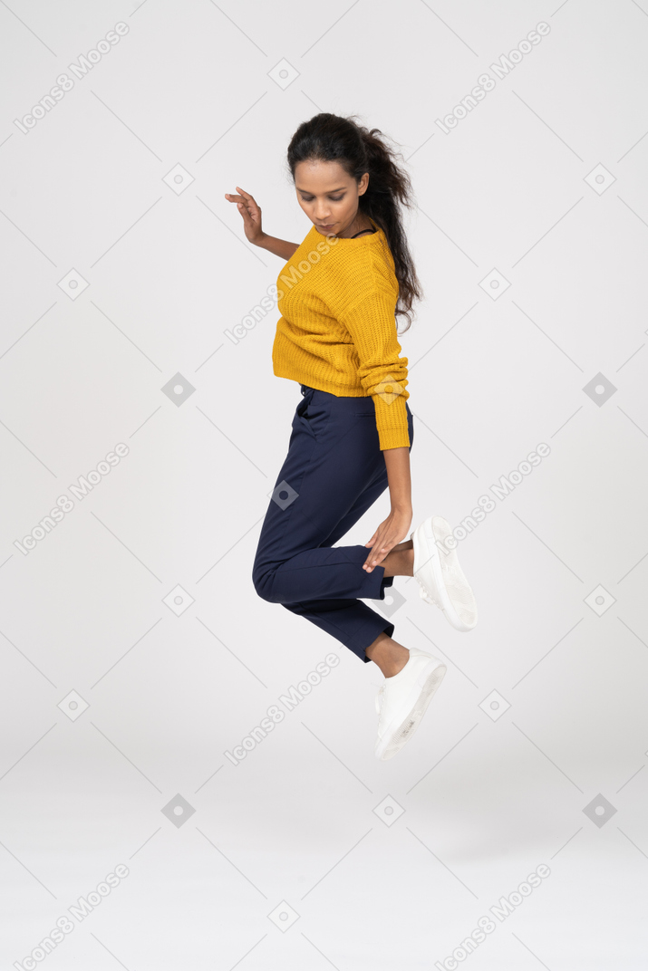 점프하고 그녀의 발을 만지는 캐주얼 옷을 입은 소녀의 측면보기
