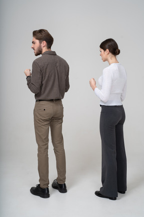 Vista posteriore di tre quarti di una coppia furiosa in abiti da ufficio stringendo i pugni