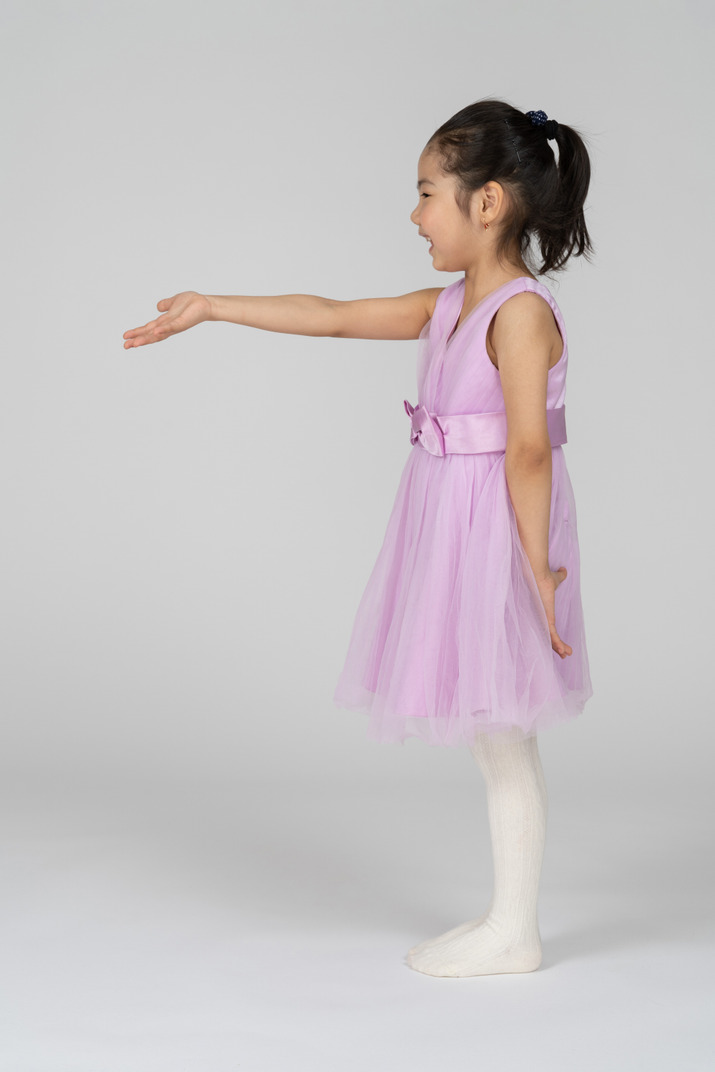 Side view of a little girl in a pretty dress reaching out her right arm