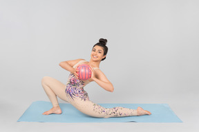 Giovane ginnasta indiana che si allunga seduta sulla stuoia di yoga e che tiene palla