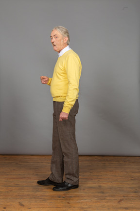 Vista laterale di un uomo anziano che parla e gesticola mentre guarda la fotocamera
