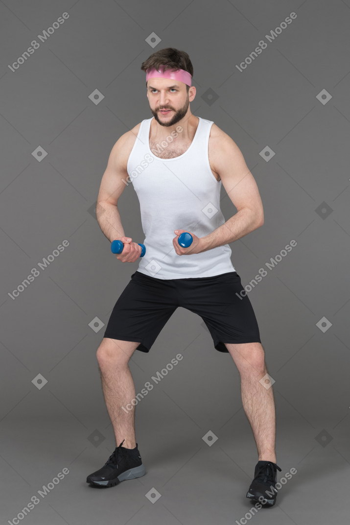 Sportlicher mann, der armübungen mit blauen hanteln macht